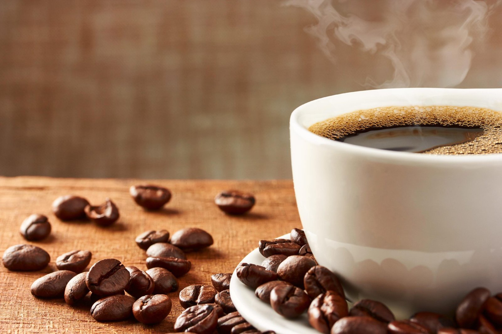 Steaming cup of coffee in a white mug, surrounded by scattered coffee beans on a warm-toned surface. Inviting, cozy atmosphere with rich aroma.
